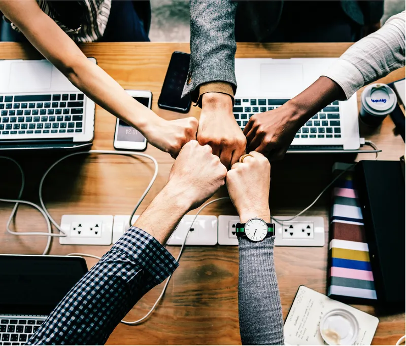 Team fist bump over a desk of laptops